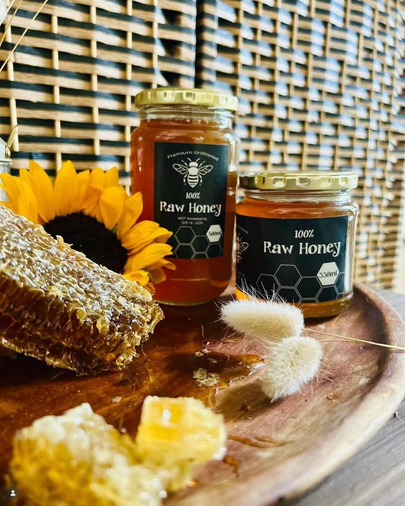 Two jars of MDP Beekeeping raw honey grouped with a piece of honeycomb and a sunflower