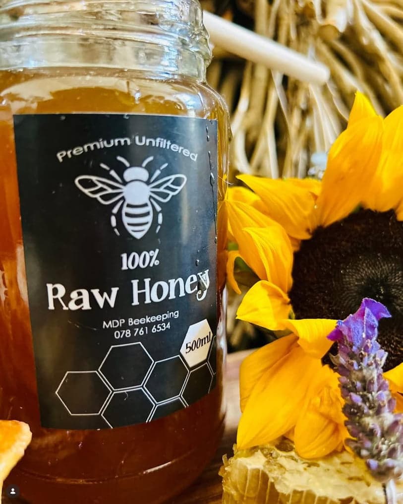 A jar of MDP Beekeeping raw honey labelled Premium Unfiltered, beside a sunflower and a sprig of lavender