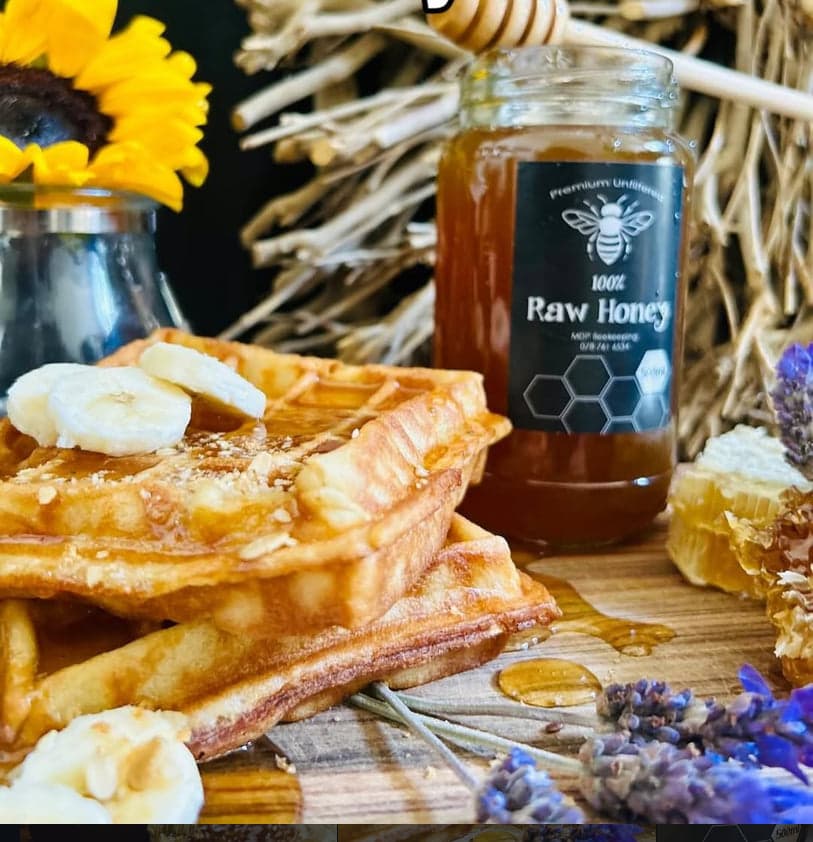 Waffles topped with banana slices and drizzled with MDP Beekeeping raw honey, beside the jar, a piece of honeycomb, and lavender sprigs